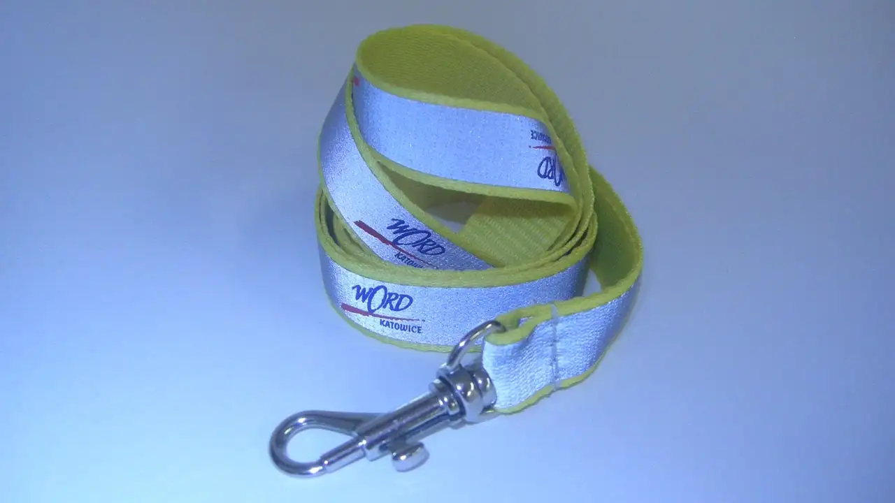 Ett gult nyckelband med påsytt blänkande reflexband och tryckt logotyp, fotograferat med blixt.